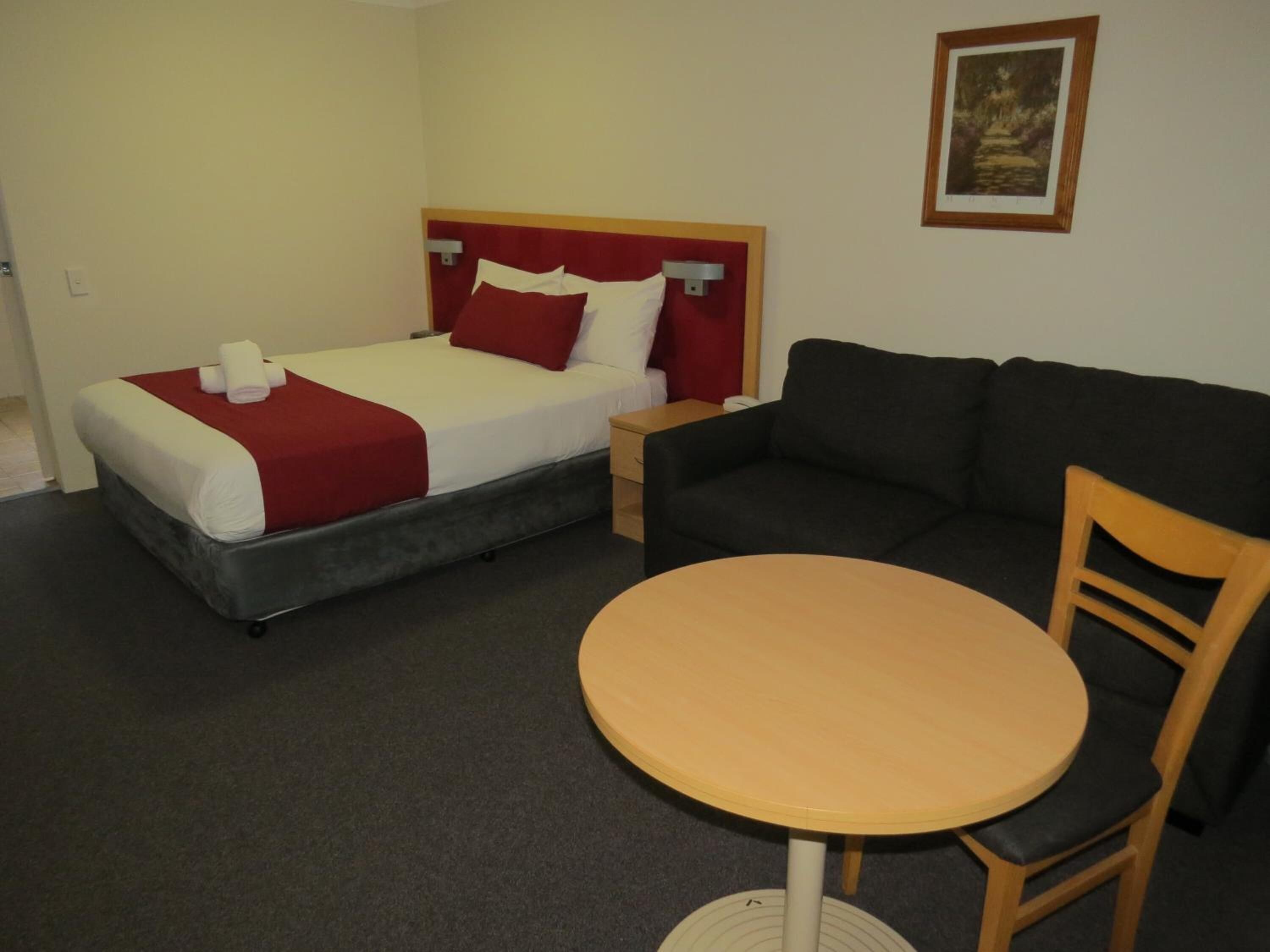A hotel room with a bed, a sofa, a table, and a picture on the wall.