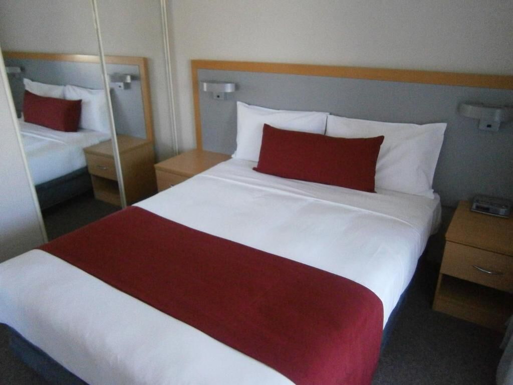 A neatly made bed with white and red bedding, a wooden headboard, and bedside tables with drawers.