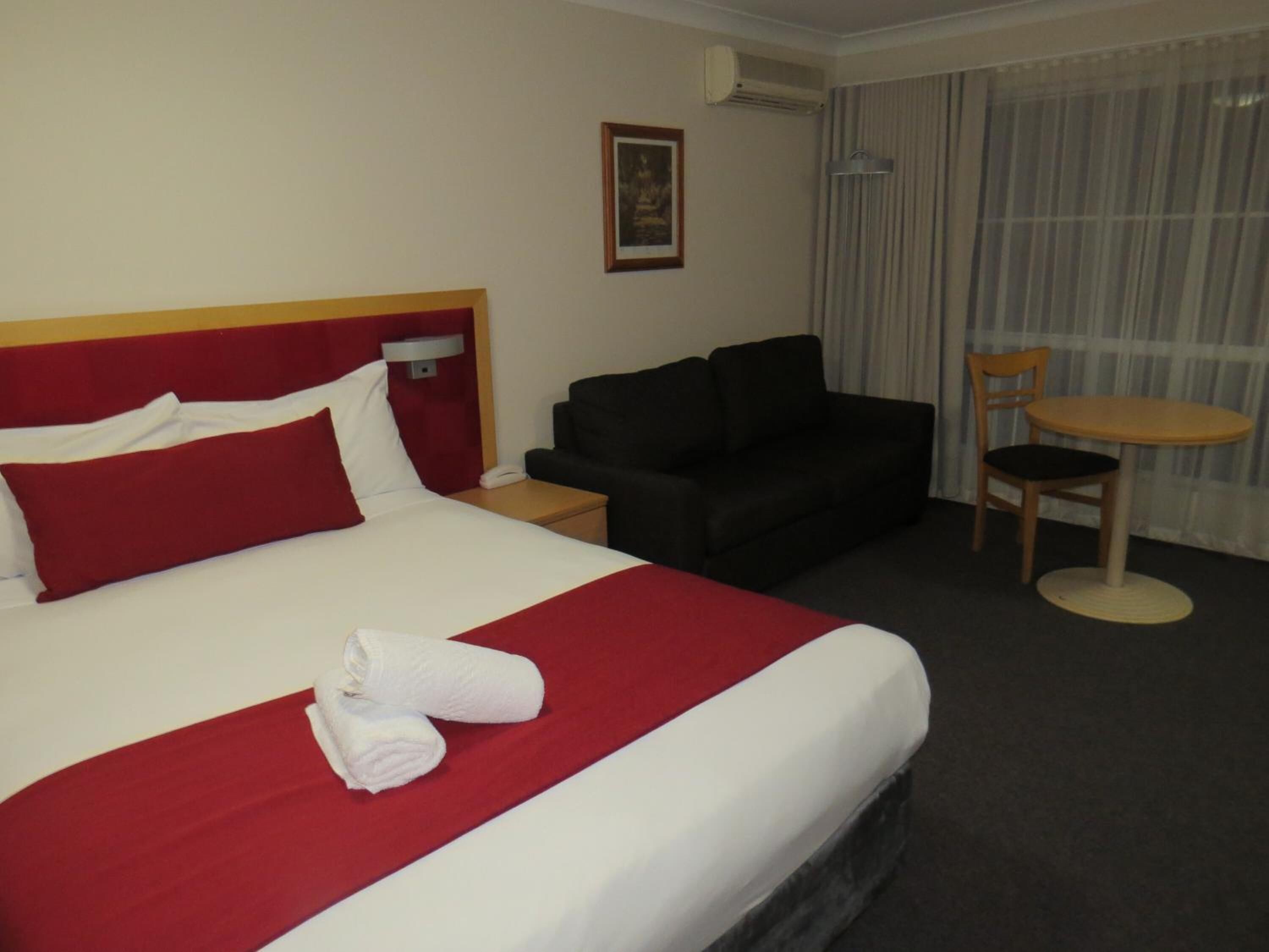 A hotel room with a large bed, a small sofa, a round table, and a chair.