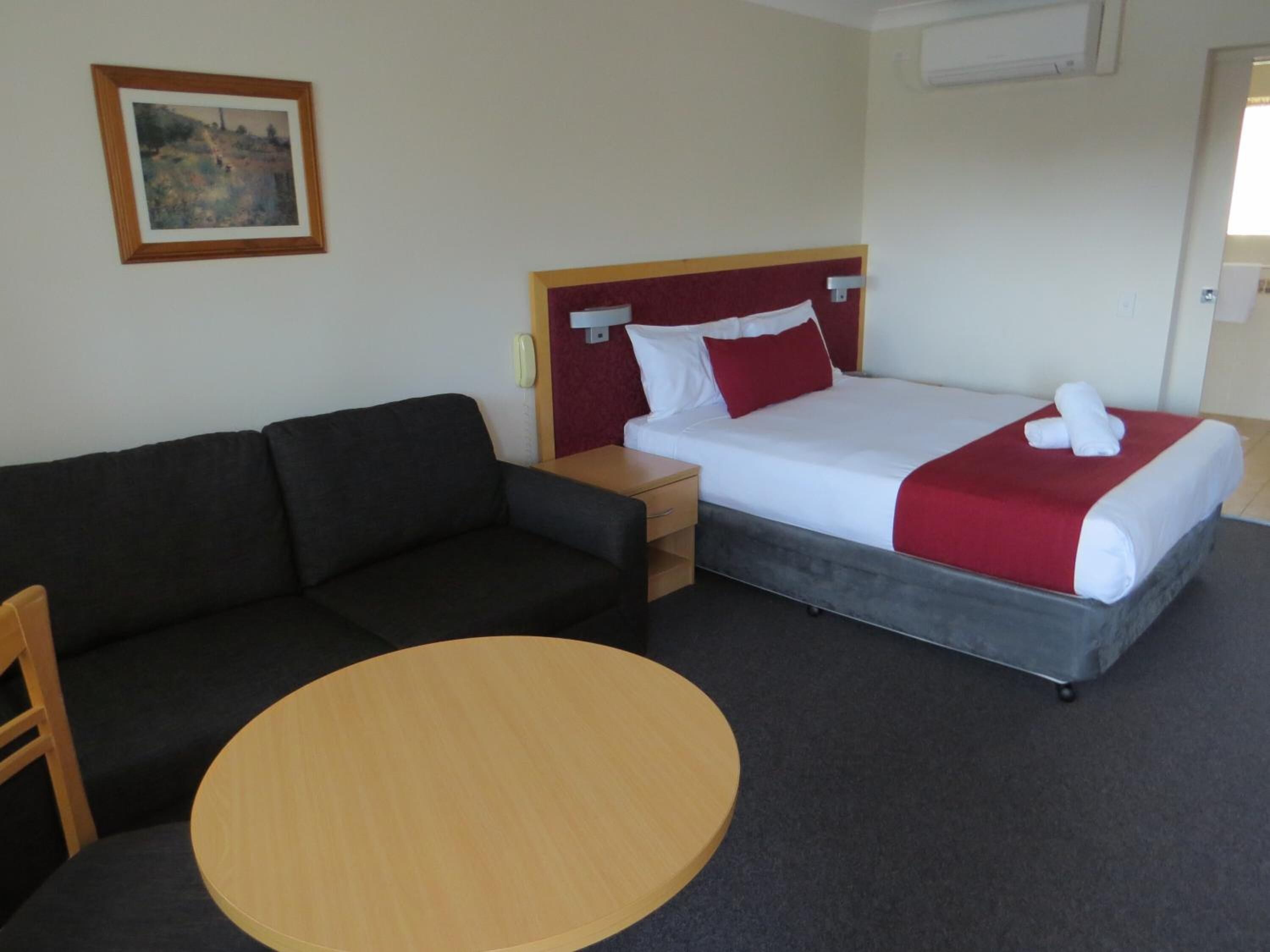 A hotel room with a bed, a sofa, a small table, and a painting on the wall.