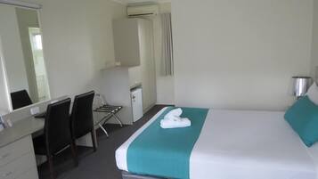 Habitación de hotel con cama, escritorio, silla, espejo y un refrigerador pequeño.