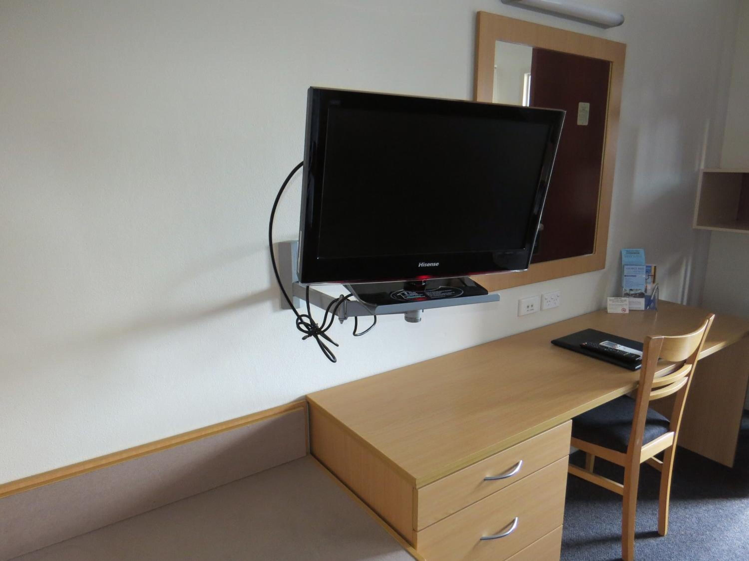 Habitación de hotel con un escritorio de madera, un televisor de pantalla plana, una silla y un espejo.