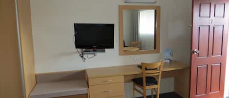 Una habitación de hotel con un escritorio de madera, un televisor, un espejo y una puerta.