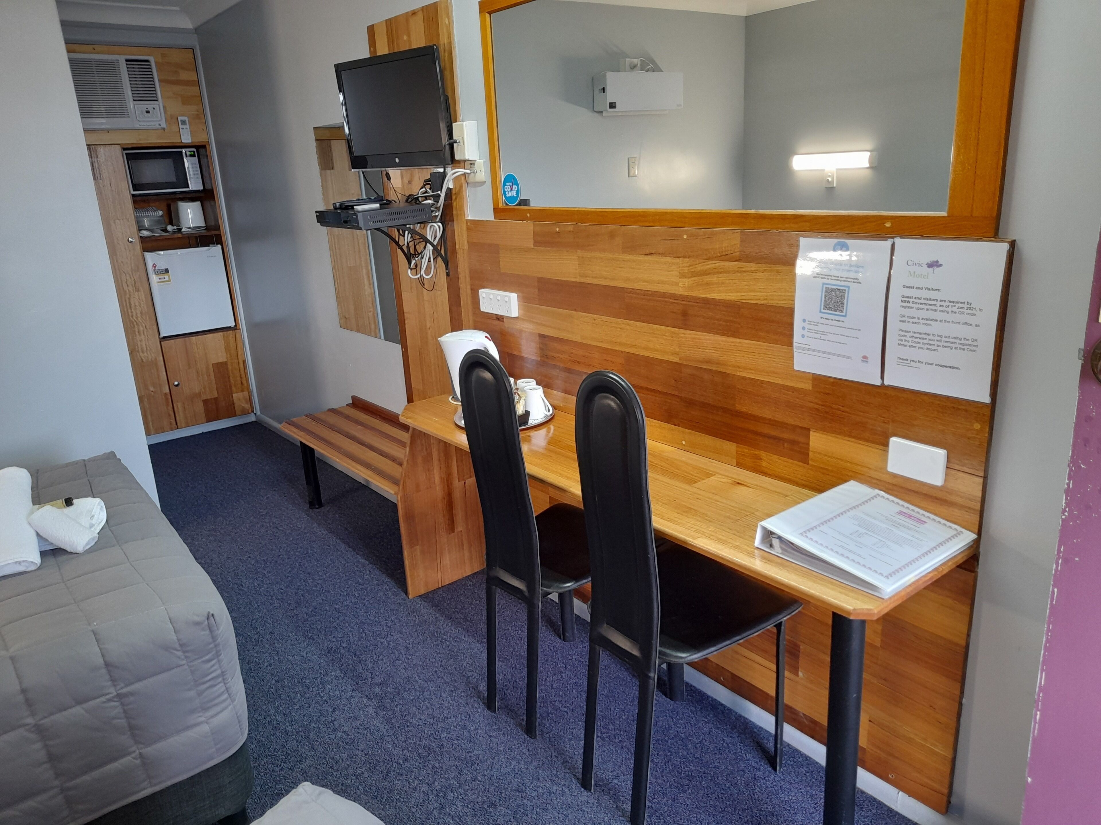 A compact hotel room with a bed, a desk with two chairs, a television, a microwave, and a small refrigerator.