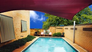 Piscina rectangular con borde de azulejos, rodeada por un muro de ladrillo y una zona cubierta con toldo rojo.