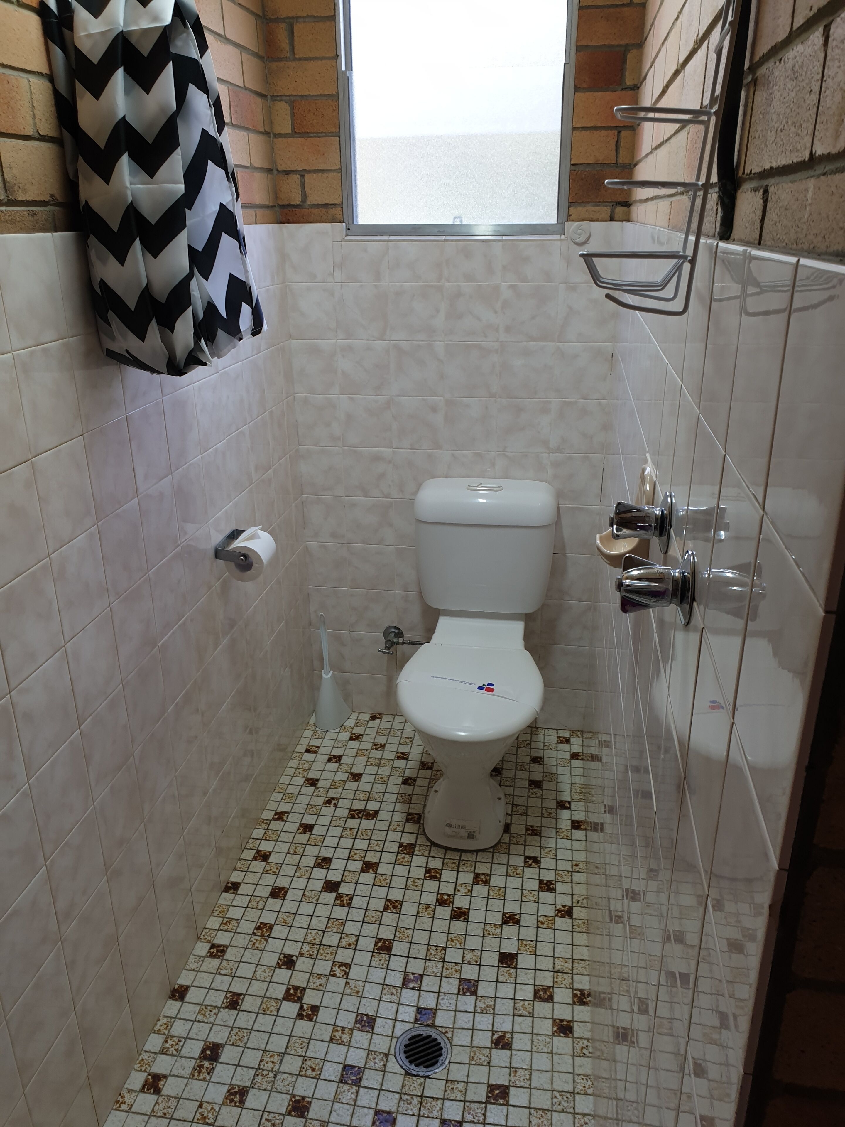 A small bathroom with a toilet, a hand dryer, and a window.