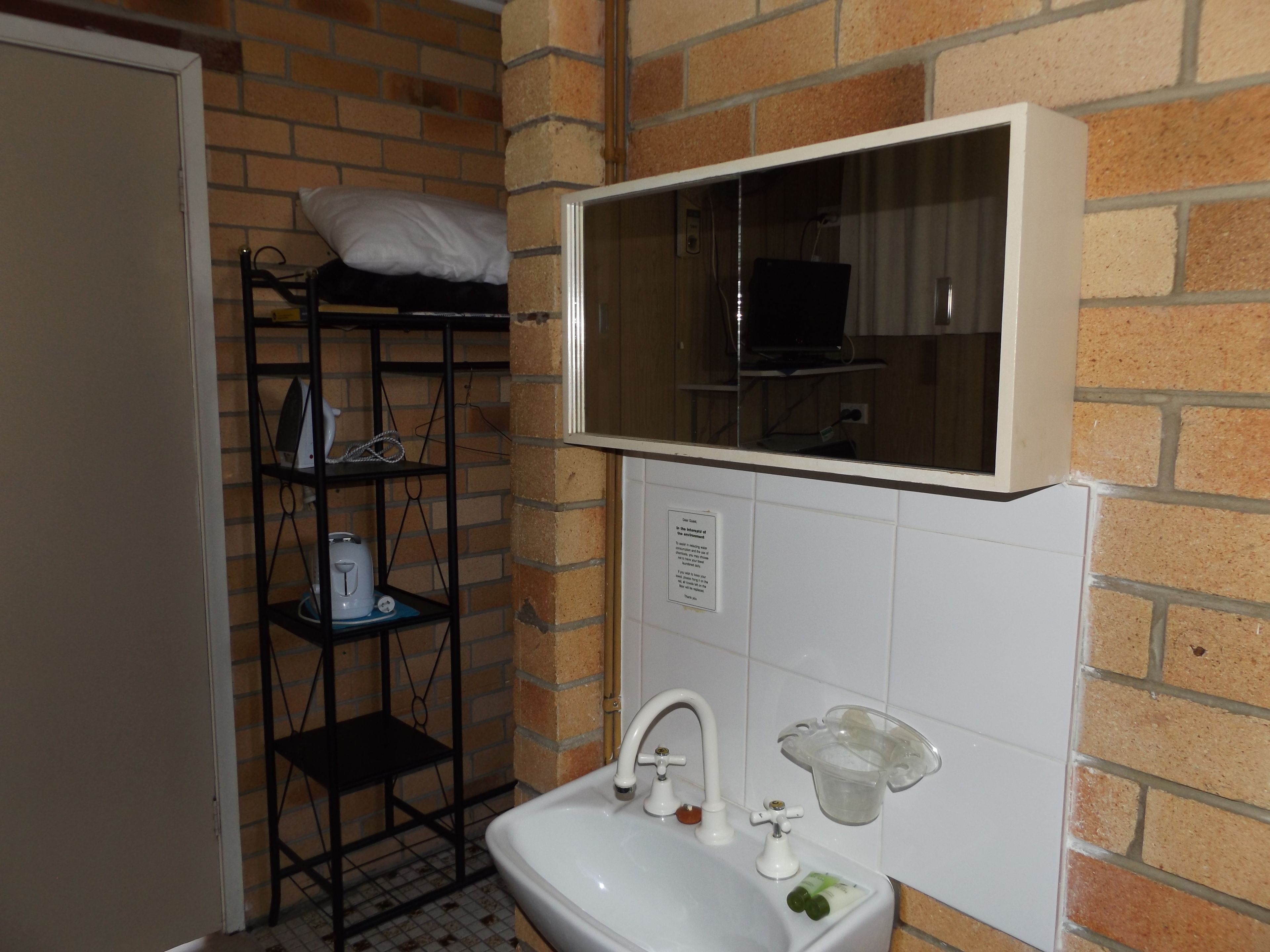 A small bathroom with a sink, mirror, and a shelf with toiletries.