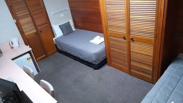 A compact room with a bed, a desk with a computer, a small refrigerator, and a wardrobe.