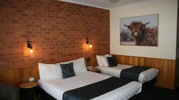 A hotel room with two beds, a brick wall, a ceiling fan, and a painting of a bull.