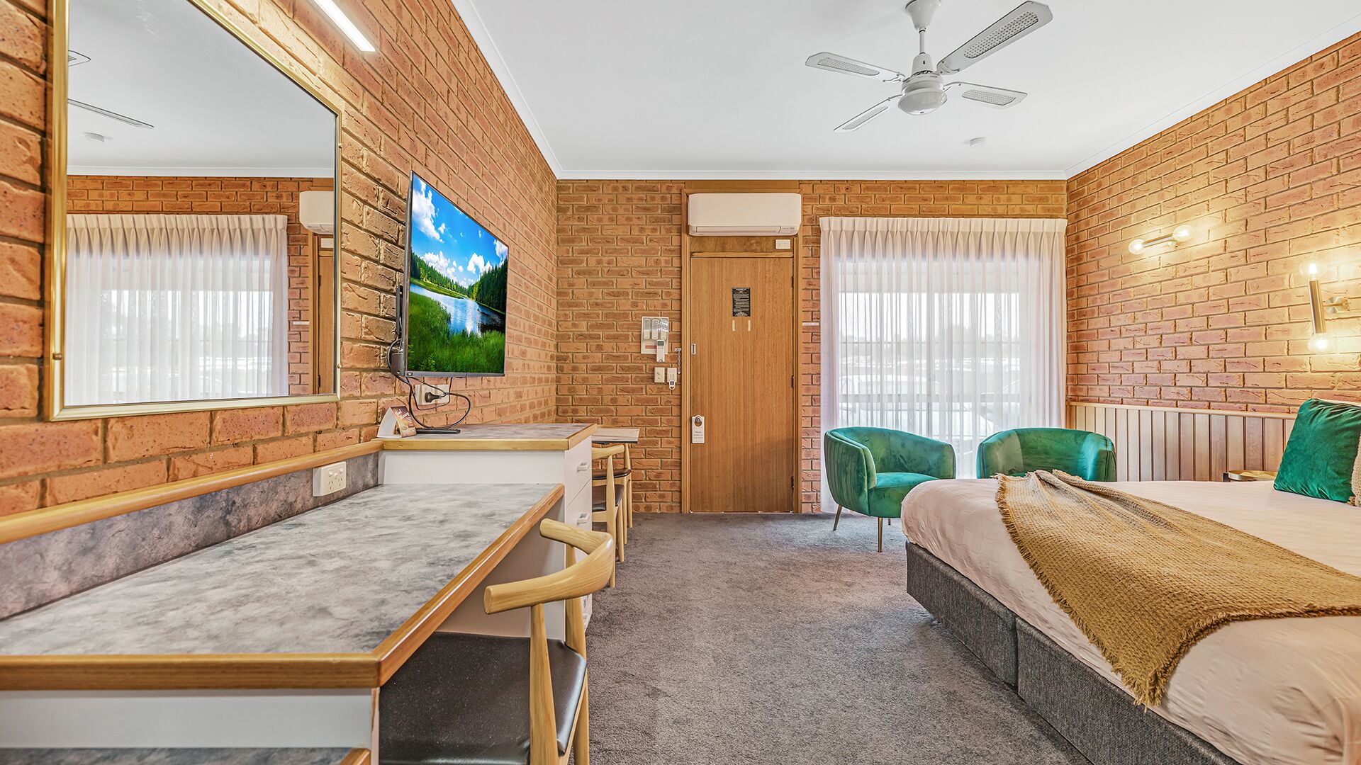 Habitación de hotel con pared de ladrillo, cama, escritorio con silla, televisión y ventilador de techo.