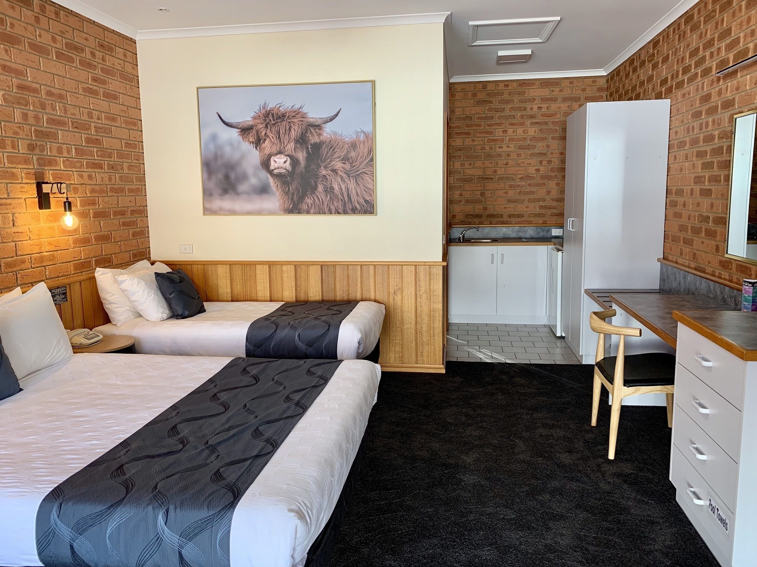 Habitación de hotel con cama, escritorio, silla, armario blanco, lavamanos y pared de ladrillo.