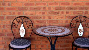 Pared de ladrillo con una mesa redonda y dos sillas de respaldo decorativo.