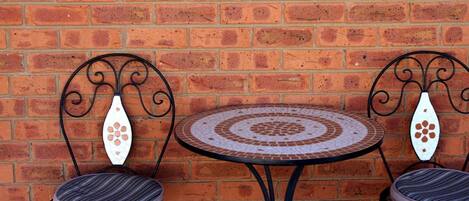 Pared de ladrillo con una mesa redonda y dos sillas de respaldo decorativo.