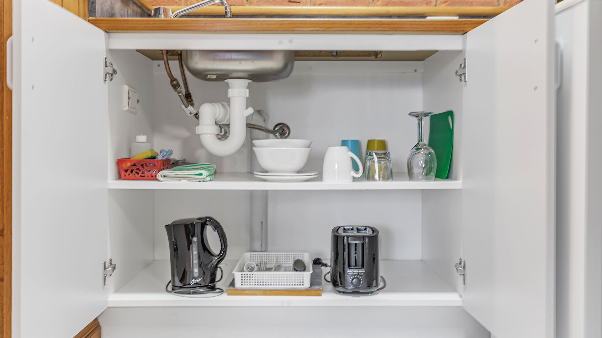 A kitchen cabinet with a sink, a kettle, a coffee maker, and various kitchen items on the shelves.