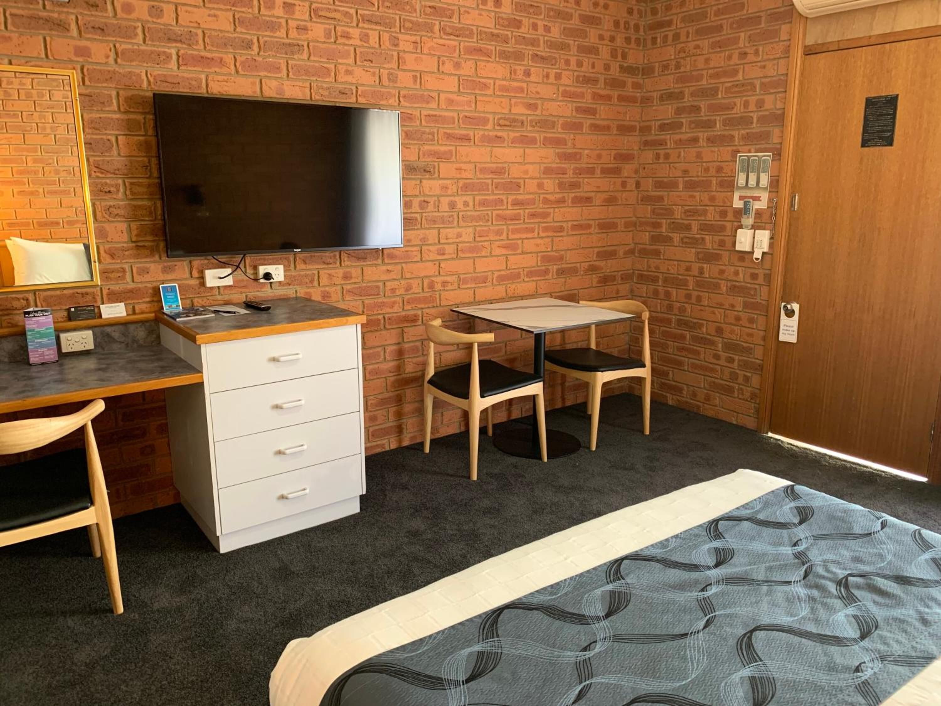 Quarto de hotel com parede de tijolos, televisão de tela plana, escrivaninha com cadeira, cama e porta com leitor de cartão.