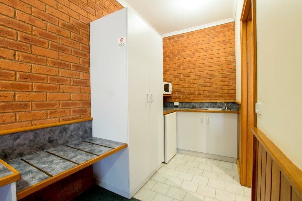 A compact kitchen with a brick wall, white cabinets, and a small countertop.