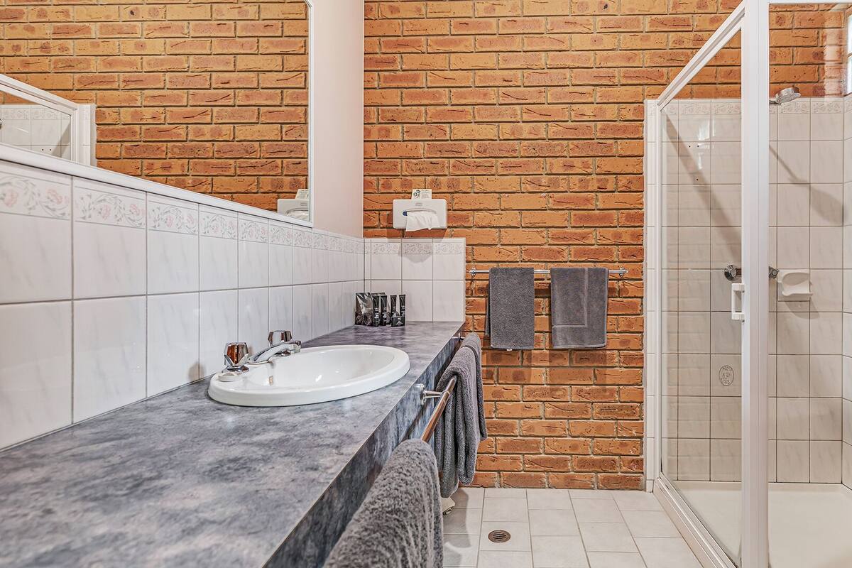 A bathroom with a marble sink, a glass shower enclosure, and a brick wall.