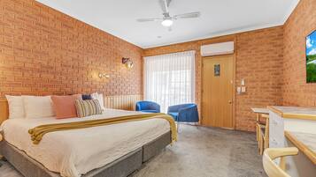 Un dormitorio con pared de ladrillo, una cama con edredón blanco, ventilador de techo y una ventana con cortinas.