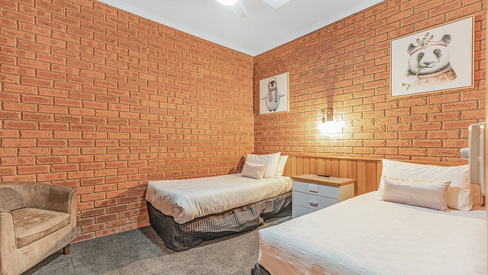 Una habitación con pared de ladrillo, dos camas, una silla y obras de arte.