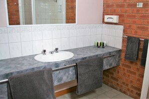A bathroom with a white sink, grey countertop, and a mirror. There are two towels hanging on the wall and a tissue box mounted on the wall.