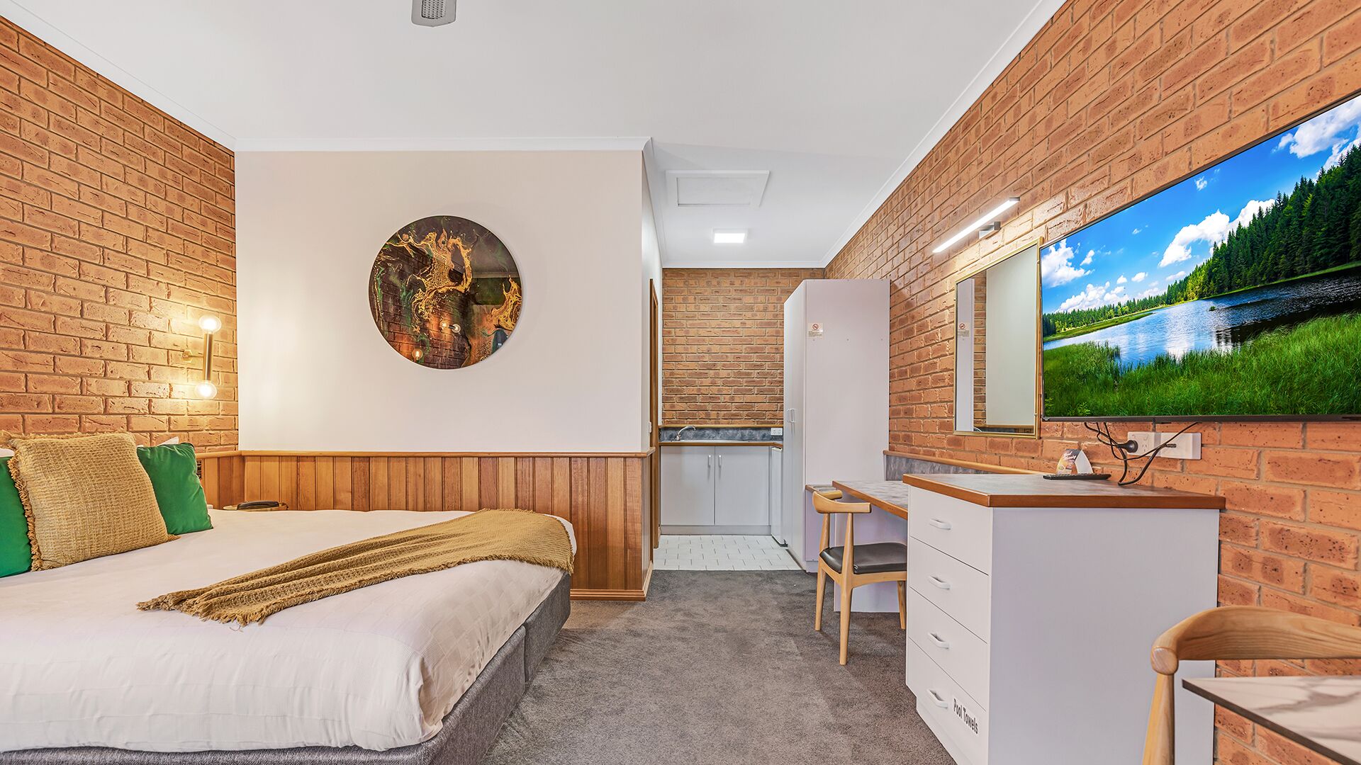 Una camera da letto con un letto, un'opera d'arte circolare appesa al muro, un angolo cottura e un bagno con uno specchio.