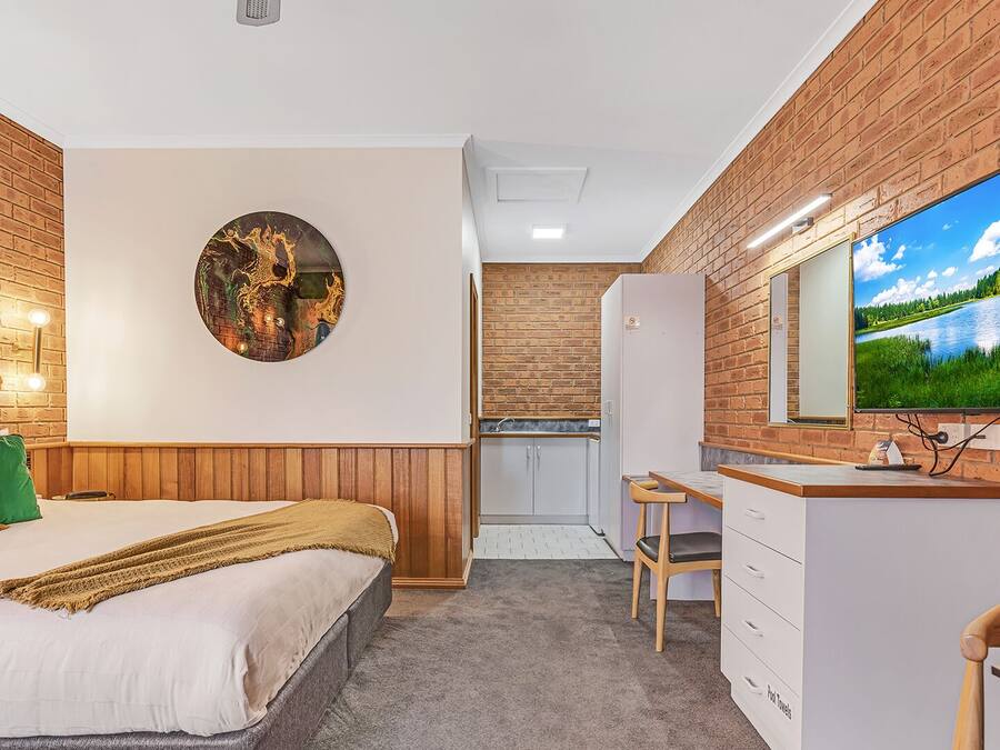 Una camera da letto con un letto, un'opera d'arte circolare appesa al muro, un angolo cottura e un bagno con uno specchio.