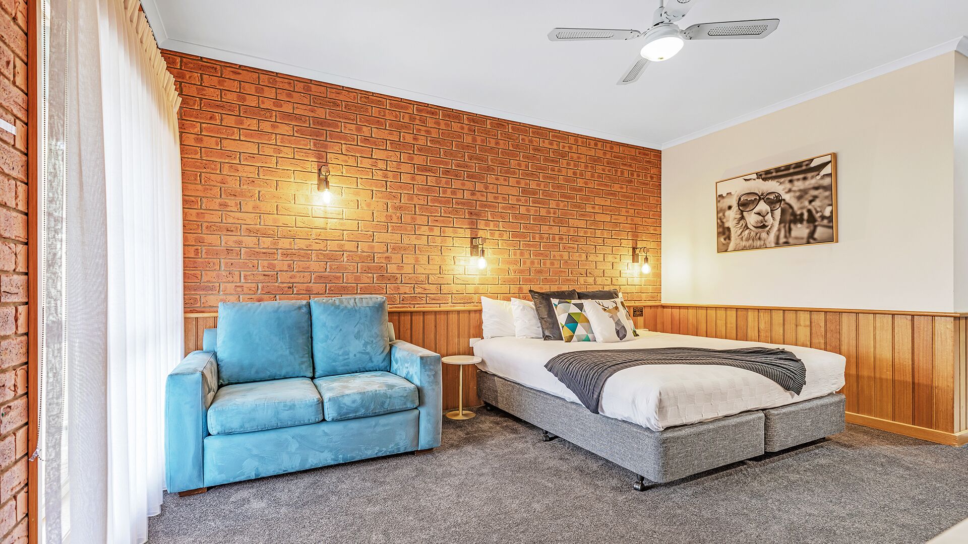 Una stanza con un muro in mattoni, un divano blu, un letto con testiera in legno e una ventola a soffitto.