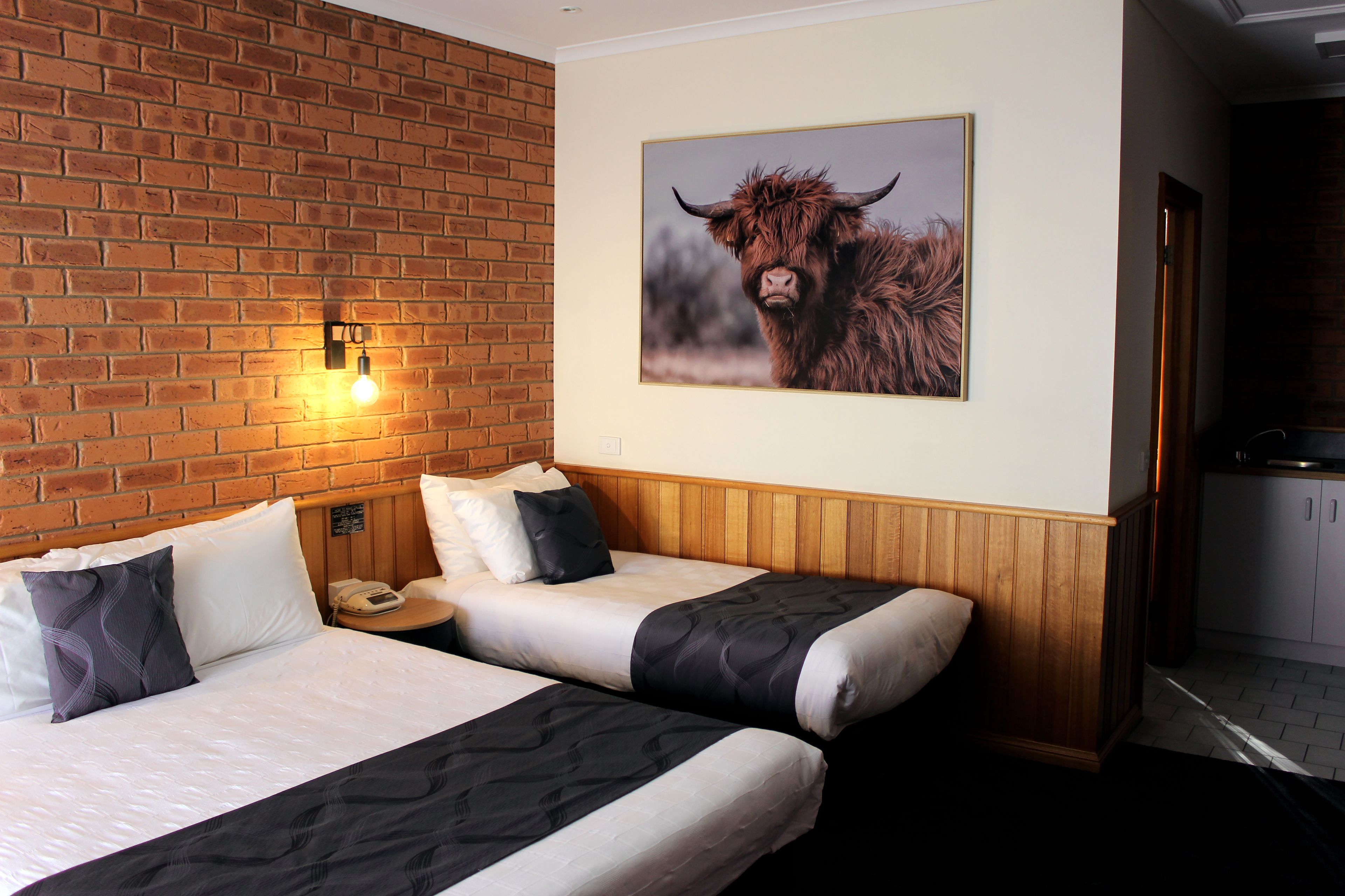 Een hotelkamer met twee bedden, een bakstenen muur, een aan de wand bevestigd beeld van een stier en een houten hoofdeinde.