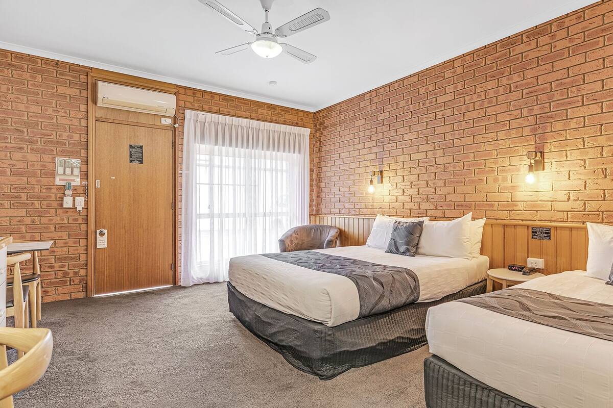 A hotel room with a brick wall, a bed, a desk, and a chair.