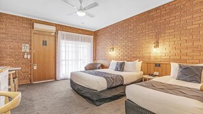 A hotel room with a brick wall, a bed, a desk, and a chair.