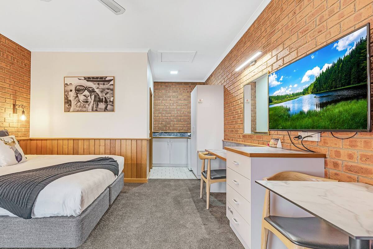A compact room with a bed, a small kitchenette, and a TV mounted on the wall.