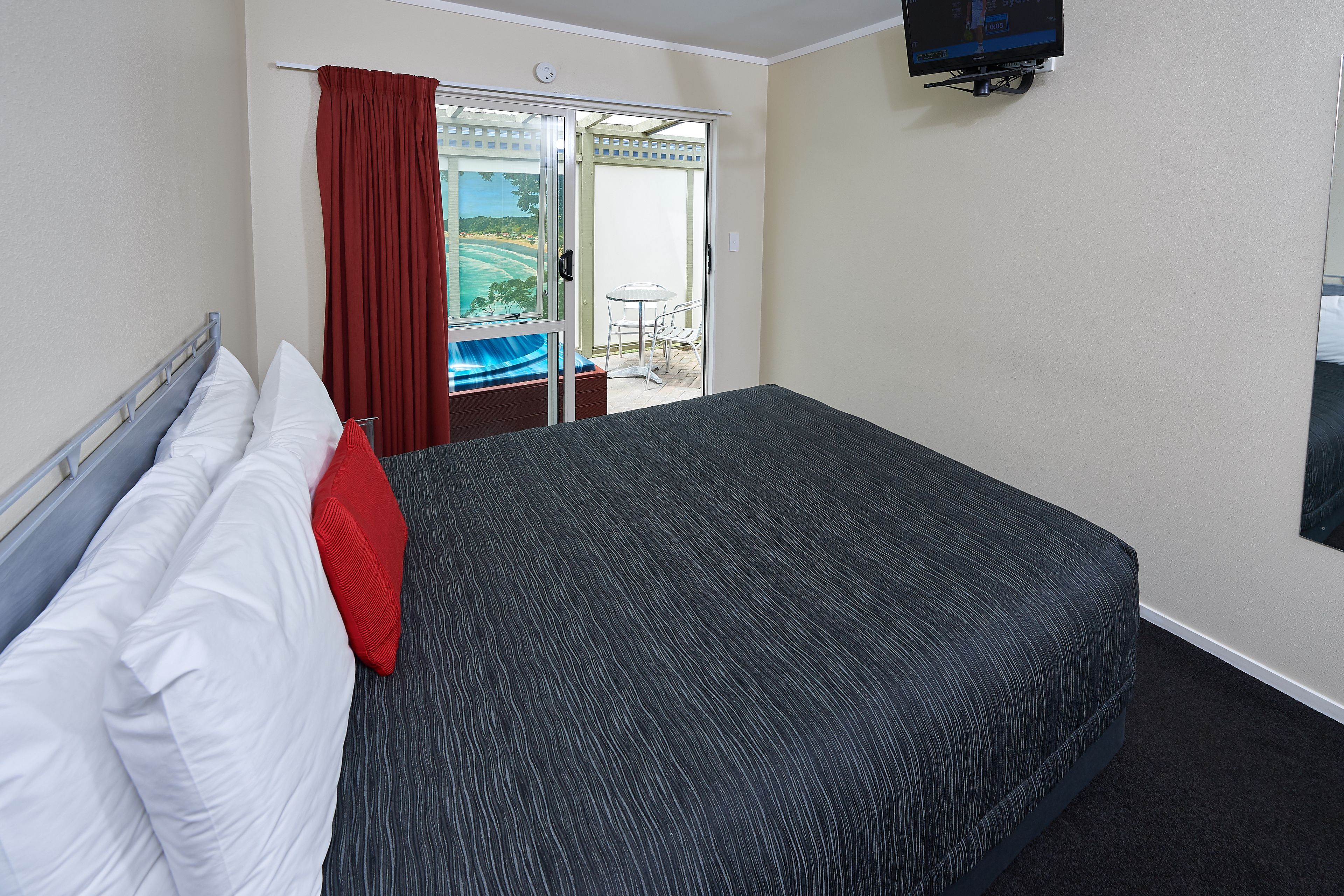 Habitación de hotel con cama, televisión, puerta corrediza a un balcón y vista a un paisaje.