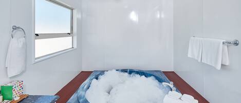 Un baño moderno con una bañera grande llena de burbujas, una ventana y un perchero.