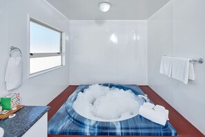 A modern bathroom with a large bathtub filled with bubbles, a window, and a towel rack. - Livingston Motel (Whakatane)