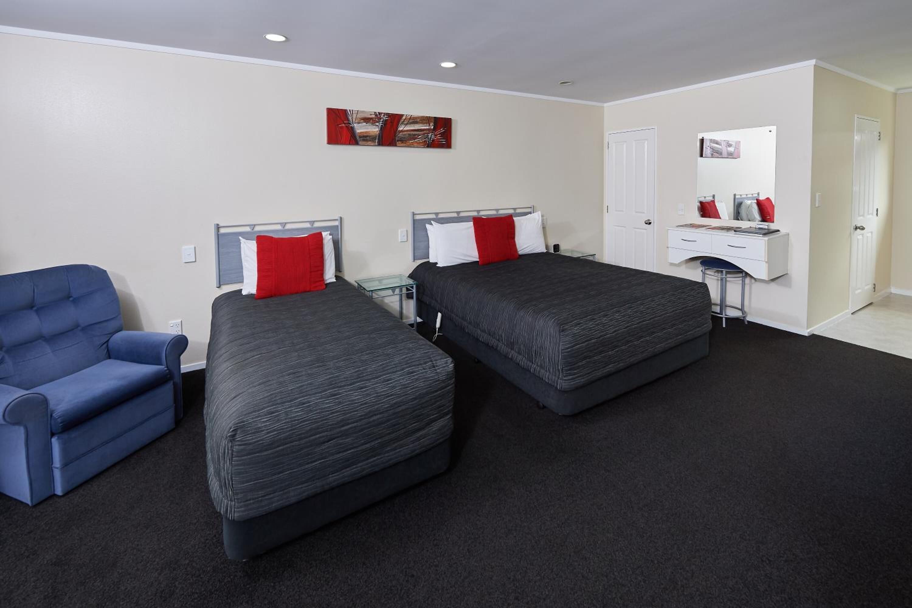 A bedroom with two beds, a blue armchair, a dresser, and a mirror.