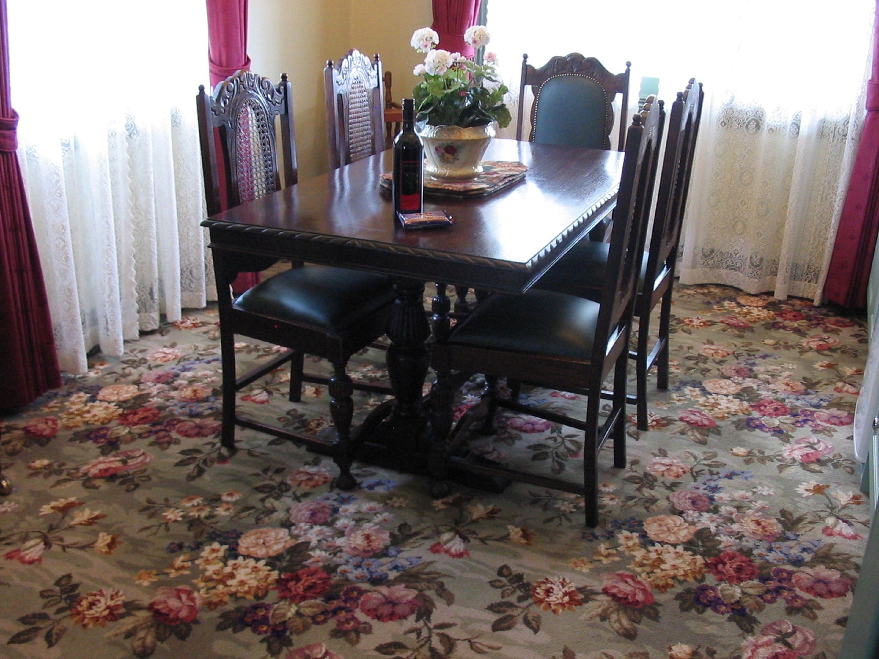 Una mesa de comedor con sillas, un florero con flores y una alfombra estampada.