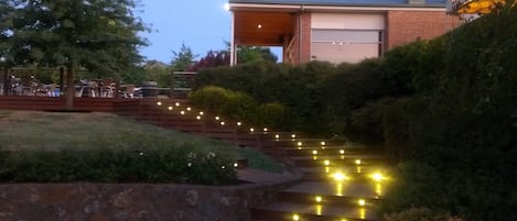 A building with a garage door, surrounded by a landscaped area with steps and string lights.