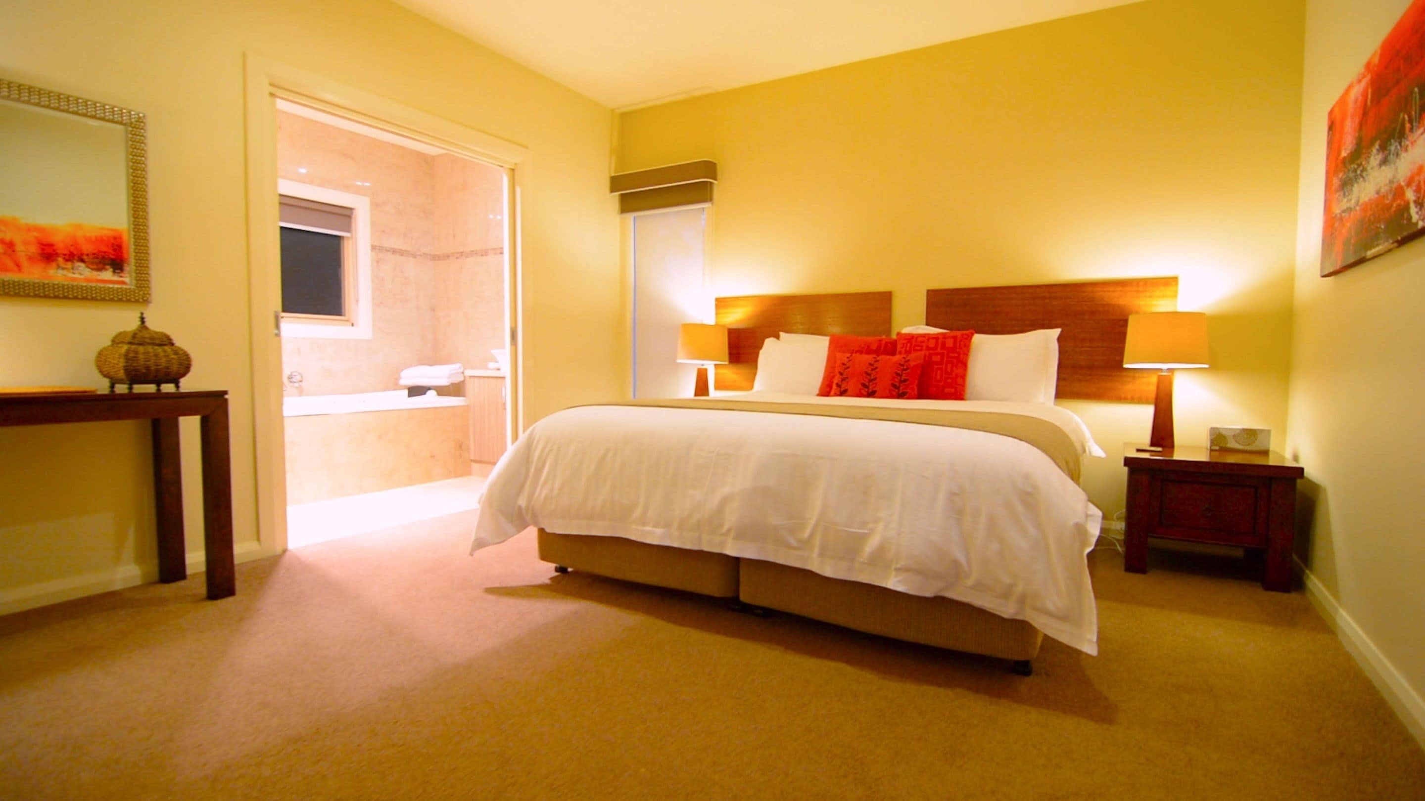 A hotel room with a large bed, bedside lamps, a nightstand, a wooden headboard, and a small table with a decorative item.