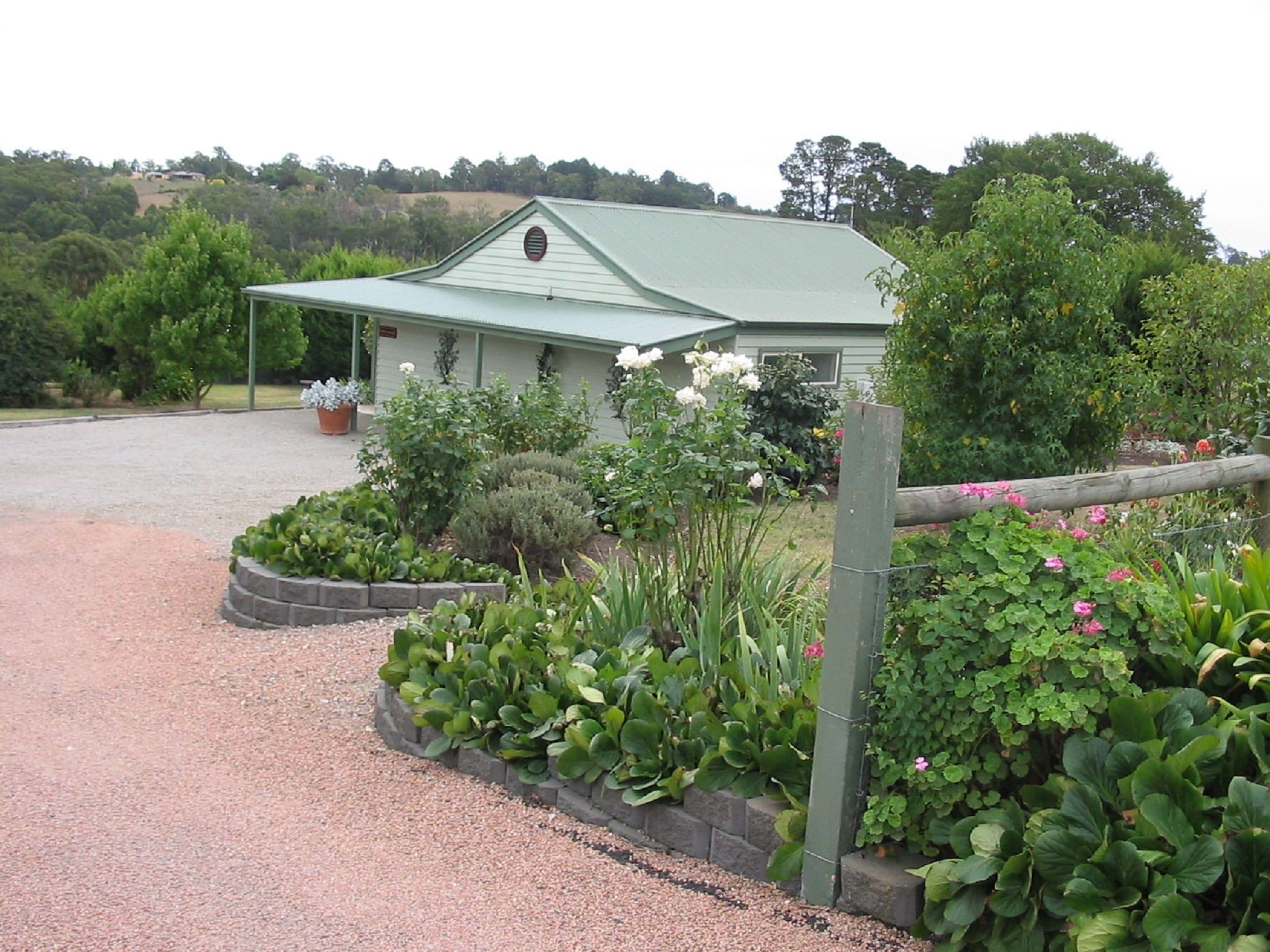 A building with a green roof, surrounded by a gravel driveway and various plants.