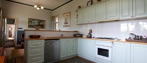 A kitchen with light green cabinets, a wooden countertop, a stove, and a dishwasher. There is a patterned rug on the floor.