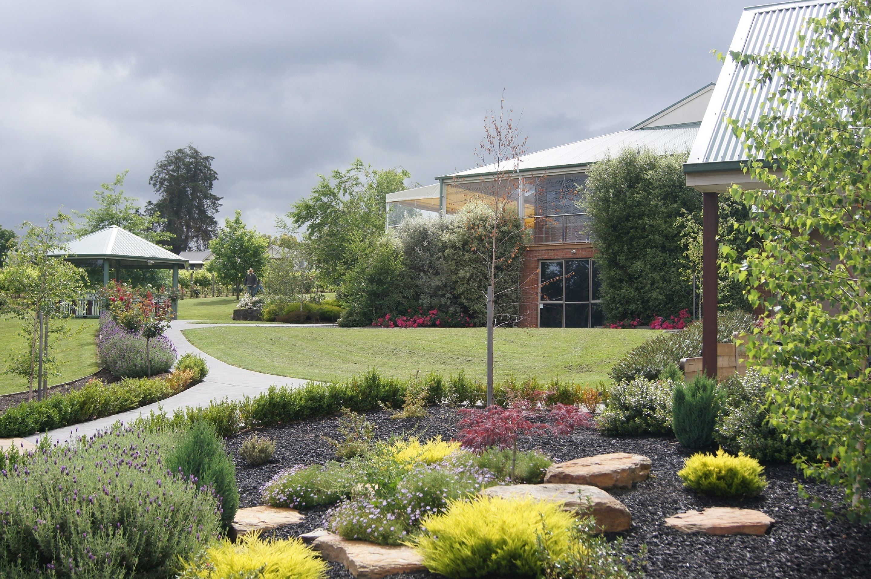 A landscaped garden with a gazebo, a modern building, and a pathway.