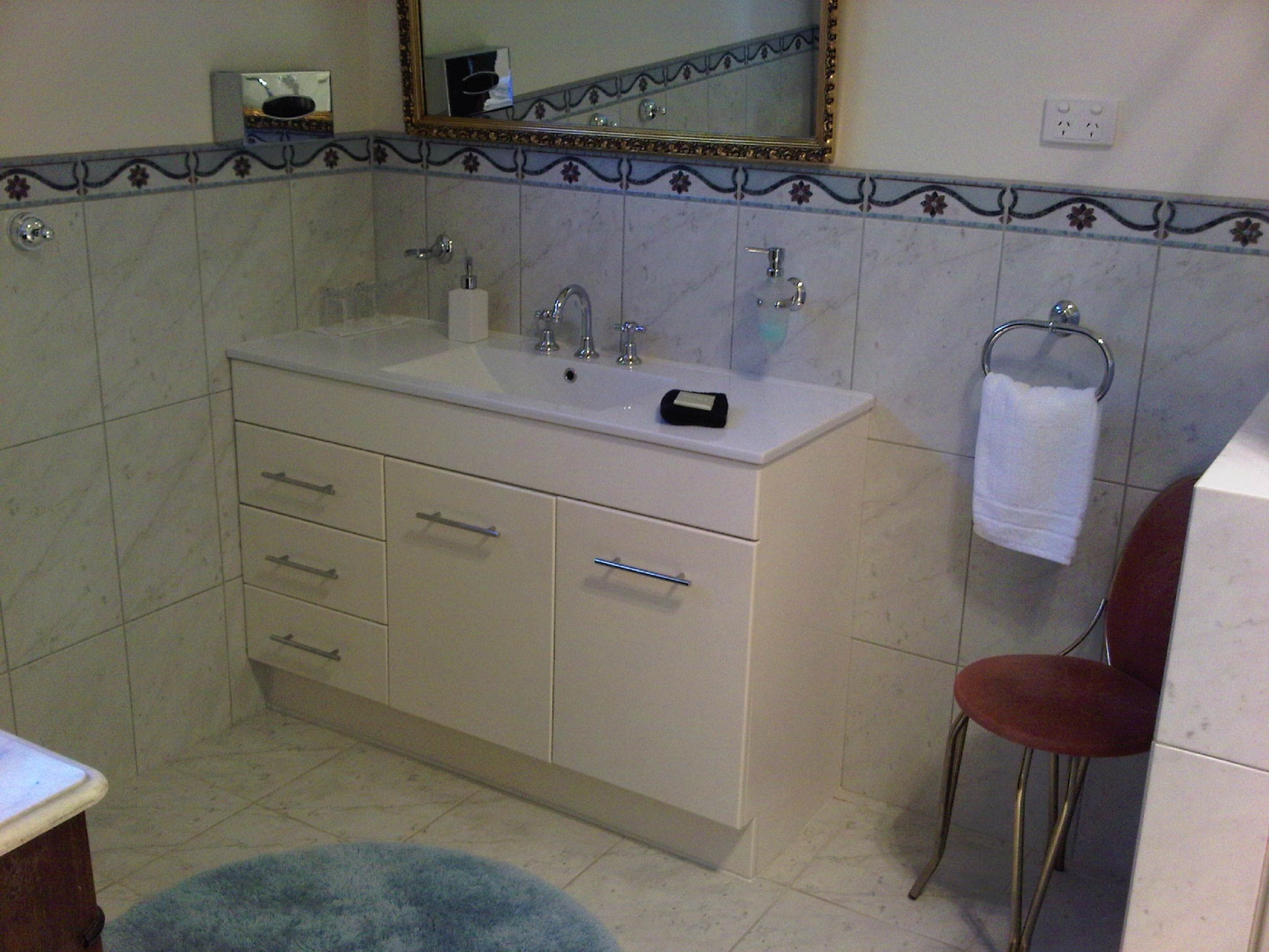 Une salle de bain avec un meuble-lavabo blanc, un miroir, un porte-serviettes et une chaise rouge.