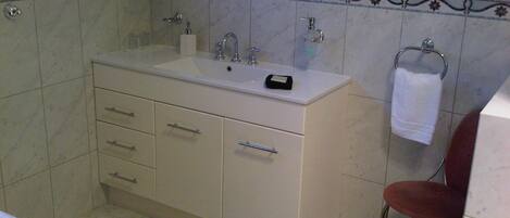 Une salle de bain avec un meuble-lavabo blanc, un miroir, un porte-serviettes et une chaise rouge.
