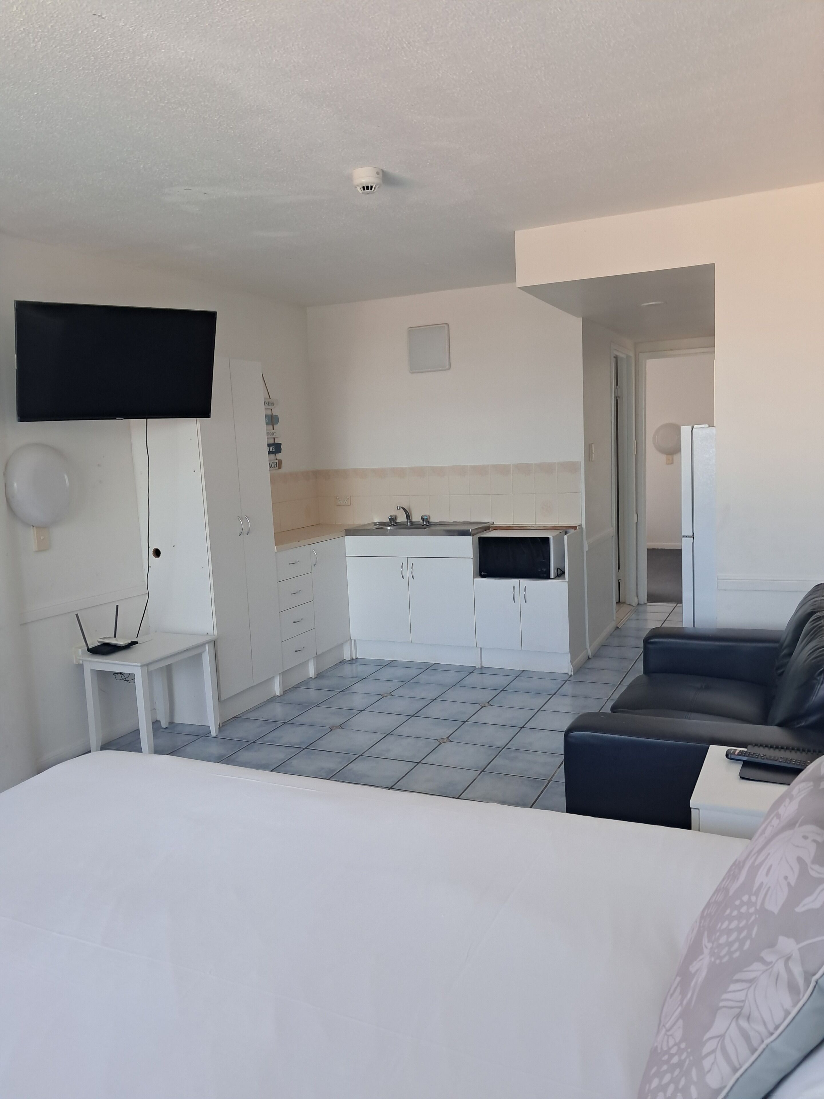 A hotel room with a bed, a TV, a small table, a desk, a kitchenette, and a sofa.