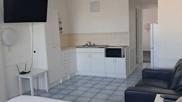 Et hotelværelse med en seng, fjernsyn, et lille bord, et skrivebord, et tekøkken og en sofa.