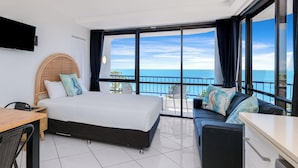 A hotel room with a bed, a sofa, a TV, a balcony with a view of the sea, and a dining area.