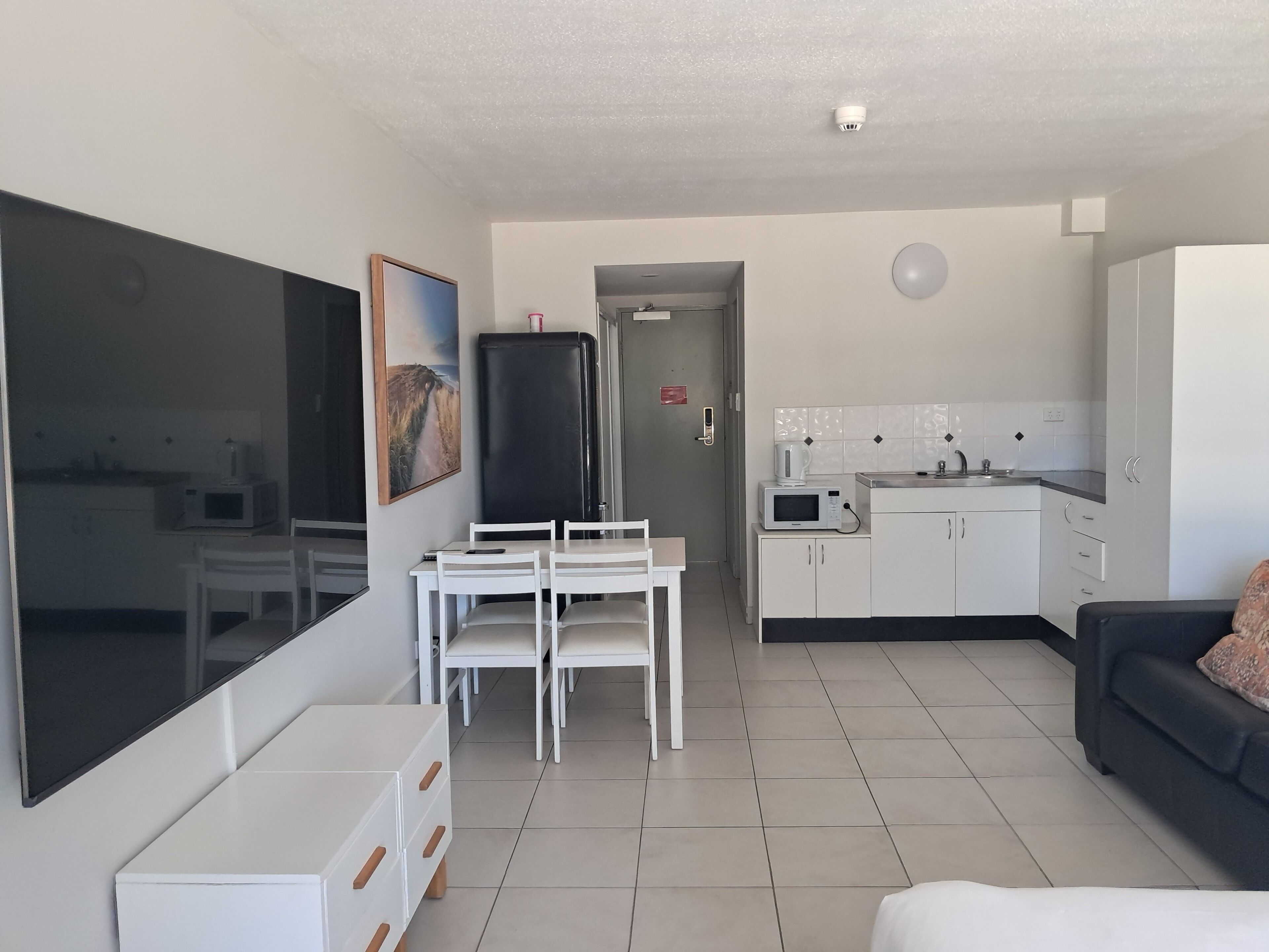Un salon moderne et bien éclairé, comprenant une table à manger, des meubles blancs, un téléviseur à écran plat et un canapé.