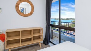 Une pièce avec une grande fenêtre, une étagère en bois, un miroir rond et un lit.