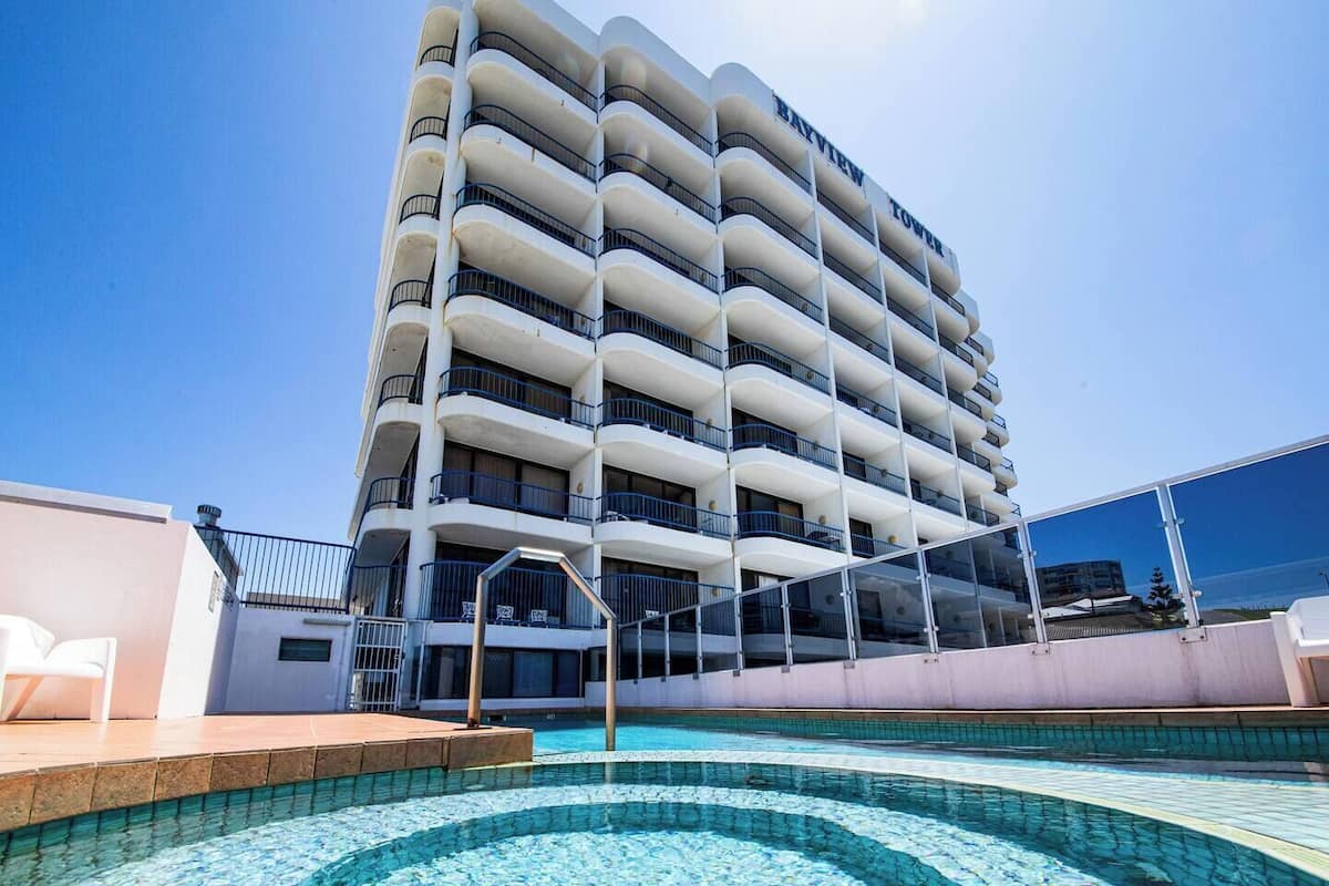 Un hotel de varios pisos con zona de piscina, balcones y cielo despejado.