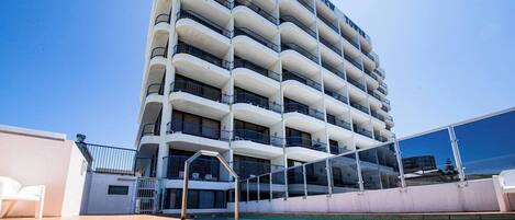Un hotel de varios pisos con zona de piscina, balcones y cielo despejado.